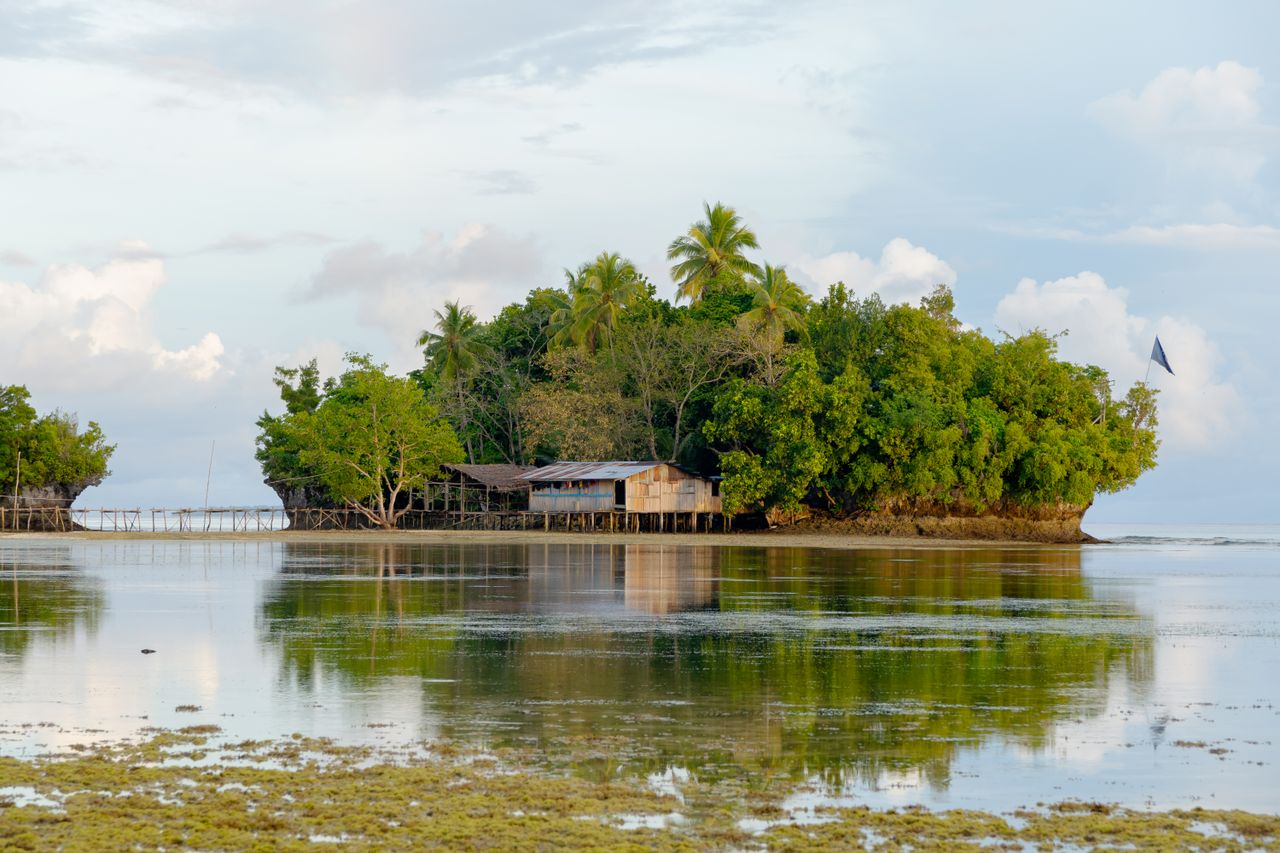 A tranquil island with lush greenery and rustic structures in Papua, Indonesia.