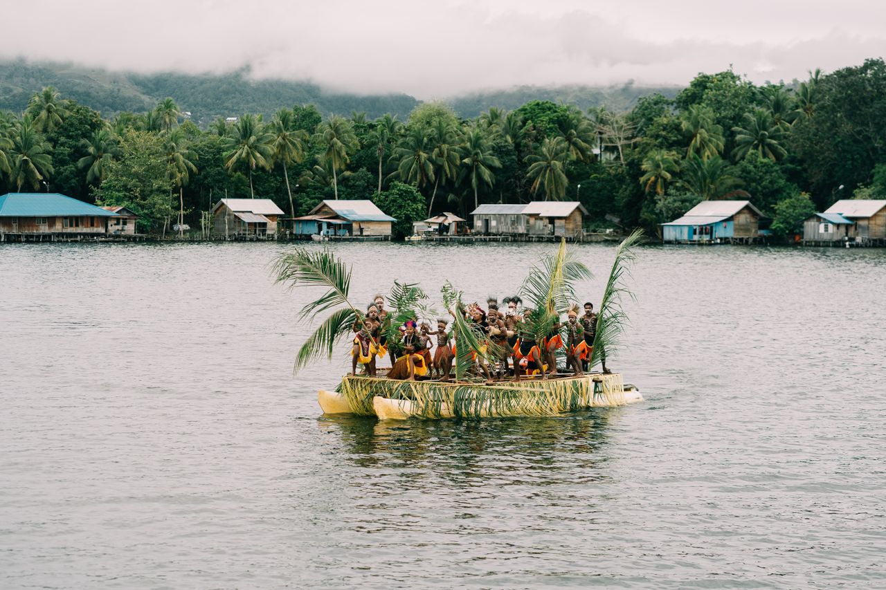 our-mission A group of people aboard a traditional boat on a serene lake in Papua, Indonesia.