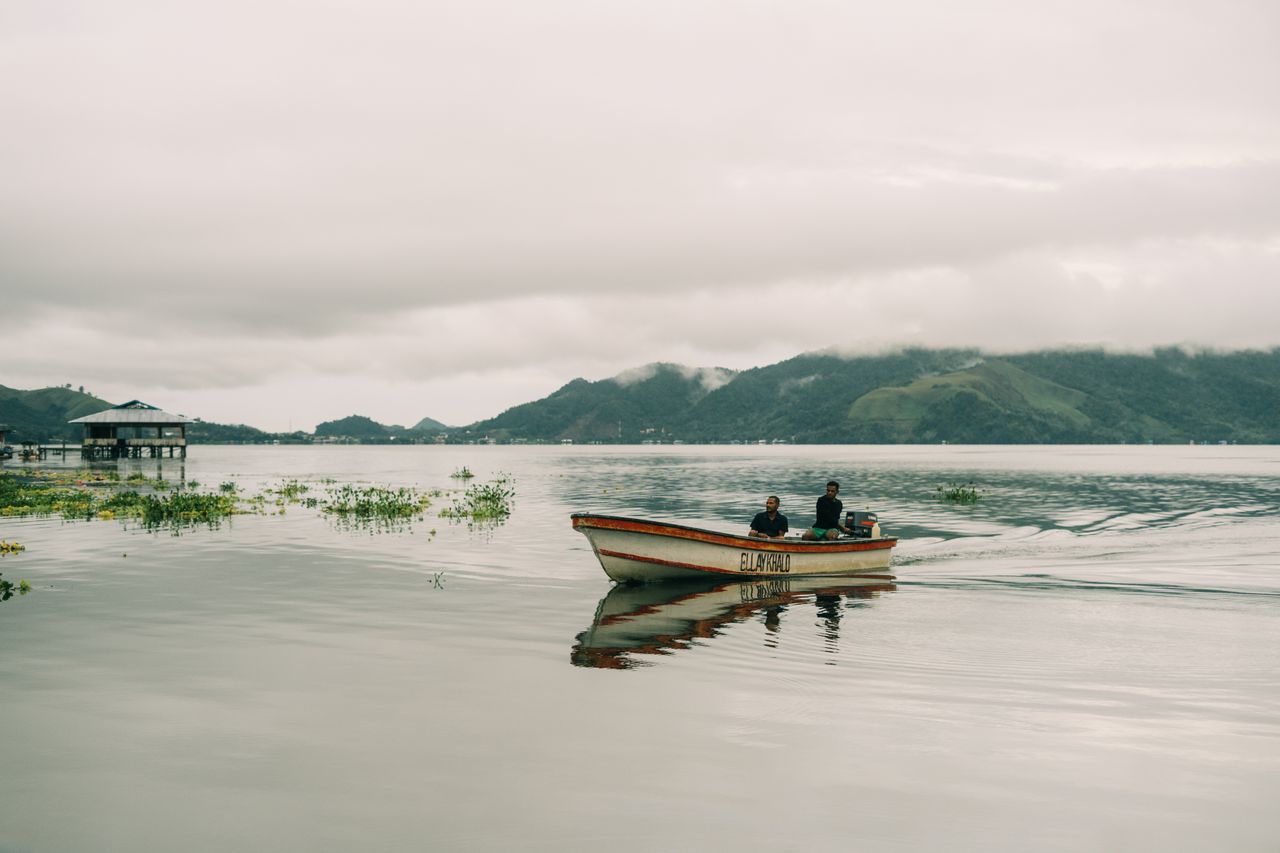 Scenes from a calm day on Lake Sentani in Papua with a motorized boat and misty mountains.